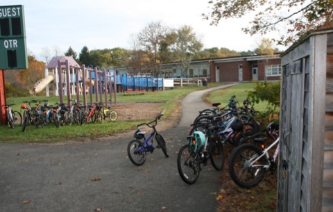 This figure is an image showing a public park path at the point where it reaches school property. Several dozen bicycles are parked at this location.
